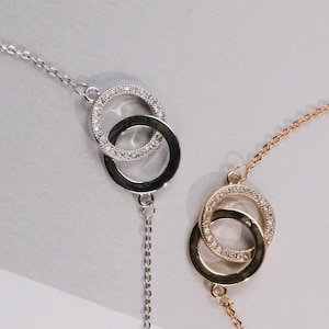May include: Two delicate necklaces, one silver and one gold, each featuring interlocking circles. The silver necklace has a chain and a circle encrusted with small, sparkling stones. The gold necklace has a similar design.