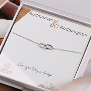 May include: A silver chain bracelet with two linked charms, each set with small clear stones. The bracelet is in a white box with the text "Godmother & Goddaughter" and "I love you today & always."