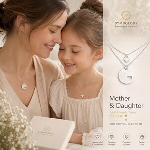 May include: A silver double-layered necklace set featuring a small heart charm on the shorter chain and a larger circular disc pendant with a heart-shaped cutout on the longer chain. The text reads Symbology Meaningful Jewellery Mother & Daughter.