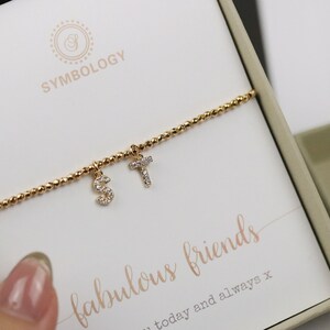 May include: Gold chain bracelet with three charms, each with a letter, S, T, and T, set with small clear stones. The bracelet is in a box with the text "fabulous friends" and "today and always x".