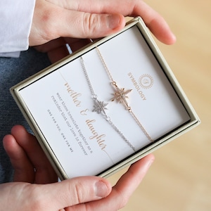 May include: Two silver and gold bracelets with a starburst charm. The bracelets are in a box with the text "mother & daughter wear these bracelets together as a reminder that our love is forever ONE FOR YOU ONE FOR ME".
