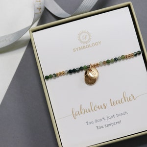 May include: A green and gold beaded bracelet with a gold charm that says "G". The bracelet is in a white box with a card that says "fabulous teacher. You don't just teach. You inspire!"