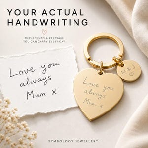 Op de afbeelding: Een goudkleurige hartvormige sleutelhanger gegraveerd met de handgeschreven tekst 'Love you always Mum x' en een kleinere ronde bedel gegraveerd met 'M & J' en een hartsymbool. De tekst 'YOUR ACTUAL HANDWRITING' is bovenaan zichtbaar.