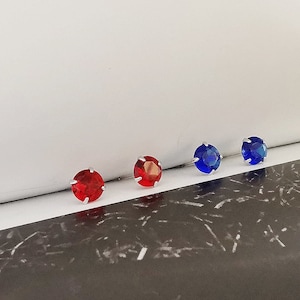 Può includere: Quattro piccoli orecchini rotondi con incastonatura a griffe. Due orecchini sono rossi e due sono blu.