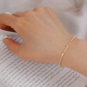 May include: A gold chain bracelet with small, clear stones. The bracelet is on a person's wrist.
