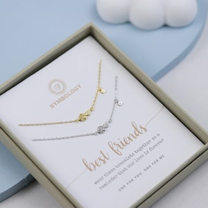 Puede incluir: Una caja blanca con un juego de pulseras de oro y plata. La caja tiene el texto "SYMBOLOGY" y "best friends". El texto dice "Usa estas pulseras juntas como un recordatorio de que nuestro amor es para siempre. UNA PARA TI, UNA PARA MÍ."