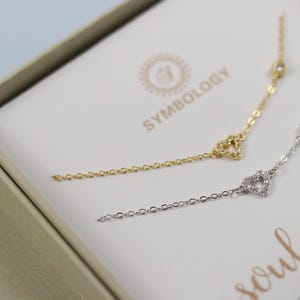 Puede incluir: Dos delicados brazaletes con dijes de corazón y pequeñas piedras de circonita cúbica. Los brazaletes están en una caja con el texto "soul sister" y el nombre de la marca "Symbology".