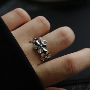 May include: A silver ring featuring a design of five interconnected flower shapes.