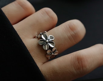 May include: A silver ring with a design of five interconnected flower shapes.
