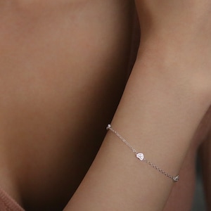 Pode incluir: Um delicado bracelete de corrente de prata com pequenos pingentes em forma de coração, cada um com uma única pedra transparente.