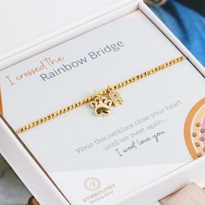 May include: A gold-toned chain necklace with a paw print charm and a letter R charm, presented in a white box. The card inside reads I crossed the Rainbow Bridge, Wear this necklace close your heart until we meet again... I woof love you.