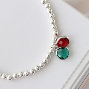 Puede incluir: Un brazalete de cuentas plateadas con un dije de cristal rojo y verde.