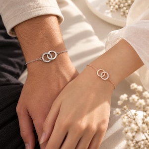Puede incluir: Dos delicadas pulseras de cadena con dijes circulares entrelazados. Una pulsera es de tono plateado con un círculo incrustado de cristales, mientras que la otra es de tono oro rosa con un círculo a juego incrustado de cristales, unidas por cadenas.