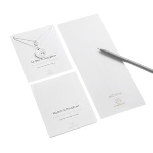May include: Two silver necklaces with heart charms on a display card labeled Mother & Daughter, with a matching card and a gray pen. The text reads Mother & Daughter, best friends from the heart, ONE FOR YOU, ONE FOR ME, and with love.
