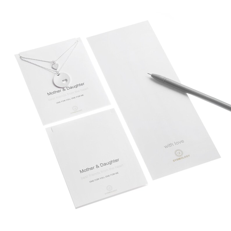 May include: Two silver necklaces with heart charms on a display card labeled Mother & Daughter, with a matching card and a gray pen. The text reads Mother & Daughter, best friends from the heart, ONE FOR YOU, ONE FOR ME, and with love.