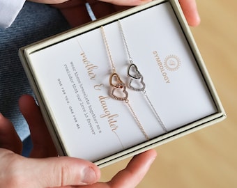 May include: Two silver and gold bracelets with interlocking heart charms. The bracelets are in a box with a card that reads "mother & daughter wear these bracelets together as a reminder that our love is forever one for you, one for me".