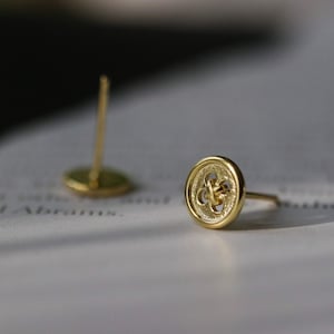 May include: A pair of gold button earrings with a detailed design. The earrings are small and delicate.
