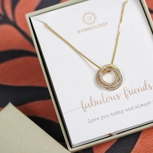 May include: A gold necklace with a pendant of three interlocking rings set with clear stones. The necklace comes in a white box with the text "fabulous friends" and "Love you today and always x".