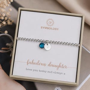 Puede incluir: Una pulsera elástica de cuentas plateadas con un pequeño dije de cristal azul y un disco plateado grabado con la letra J. La pulsera se presenta en una caja cuadrada con una tarjeta impresa con Symbology, fabulous daughter y Love you today and always x.
