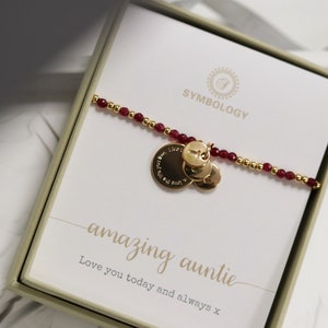 Peut inclure: Un bracelet en or avec des perles rouges et trois breloques dorées. Les breloques portent les mots "Love you today and always" gravés dessus. Le bracelet est dans une boîte avec les mots "amazing auntie" et "Love you today and always x" imprimés dessus.