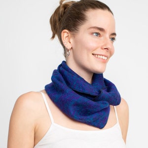 May include: A woman wearing a white tank top and a blue and purple patterned infinity scarf.