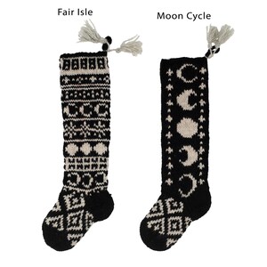 May include: Two pairs of black and white knitted socks with tassels. The socks on the left have a Fair Isle pattern. The socks on the right have a moon cycle pattern.