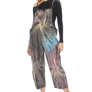 May include: A gray tie-dye jumpsuit with a black long-sleeved shirt underneath. The jumpsuit has a loose fit and features a swirling tie-dye pattern in shades of blue, pink, and white.