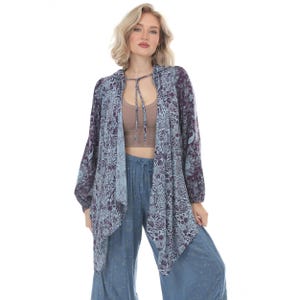 May include: A long-sleeved, open-front cardigan featuring a dark purple and light blue floral pattern, a hood, and thin tie strings at the neckline. The garment is worn over a solid tan crop top and loose-fitting blue trousers with a subtle print.