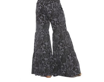 May include: Black and gray flared trousers featuring a repeating pattern of various mushrooms and circular botanical designs. The pants have a high-waisted fit and a tiered, wide-leg silhouette that extends down to the floor in a loose, flowing style.