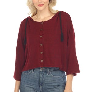 Può includere: Un maglione con cappuccio color borgogna con chiusura a bottoni sul davanti e lacci neri. Il maglione ha una lunghezza corta e una vestibilità rilassata.