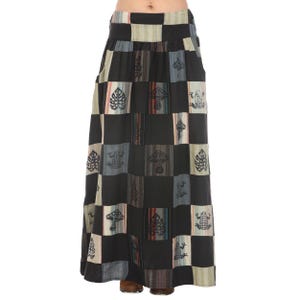 May include: A long black skirt with a patchwork design featuring frogs, mushrooms, and leaves. The skirt has a wide waistband and pockets on the sides.