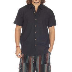 Può includere: Una camicia nera a maniche corte con bottoni e vestibilità rilassata. La camicia è abbinata a pantaloncini cargo a righe.