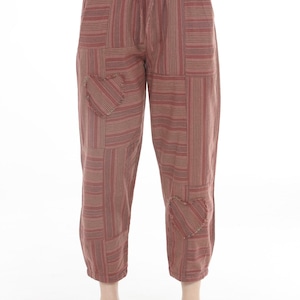 May include: These ankle-length pants feature a patchwork design in shades of rust, brown, and cream with vertical and horizontal stripes. The garment includes an elastic drawstring waistband and two heart-shaped patches with frayed edges.
