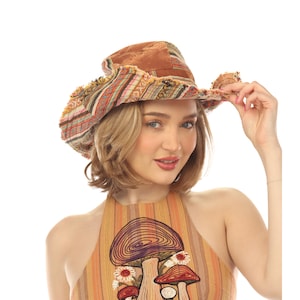 May include: A brown velvet bucket hat with a frayed brim featuring a multi-colored woven pattern of stripes and geometric shapes. The hat is paired with a sleeveless top in shades of orange and tan, decorated with a graphic of mushrooms.