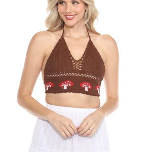 May include: A brown halter top with a crochet design. The top features a pattern of red and white mushrooms along the bottom. The top is paired with a white skirt.