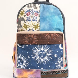May include: A patchwork backpack with a blue, brown, and white sun and star pattern. The backpack has a variety of fabric textures and colors, including a floral pattern, a tie-dye pattern, and a geometric pattern.