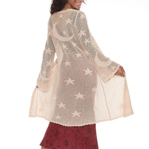 May include: A beige crochet cardigan with a moon and stars pattern. The cardigan has long sleeves and a flowy silhouette.