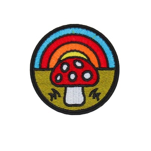 May include: A round embroidered patch featuring a red mushroom with white spots, a rainbow, and a green field. The patch has a black border and is likely for clothing or accessories.