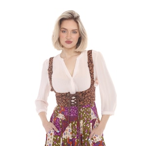 May include: A white long-sleeved blouse with a pleated front paired with a brown corset featuring a dark leaf pattern and front lace-up closure, worn over a multi-colored patchwork skirt with various floral and mushroom prints.