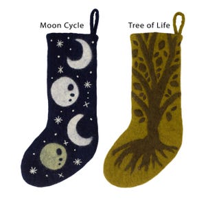 May include: Two felt Christmas stockings, one blue with a white moon cycle design and the other green with a brown tree of life design. The stockings are both hanging from a white background.