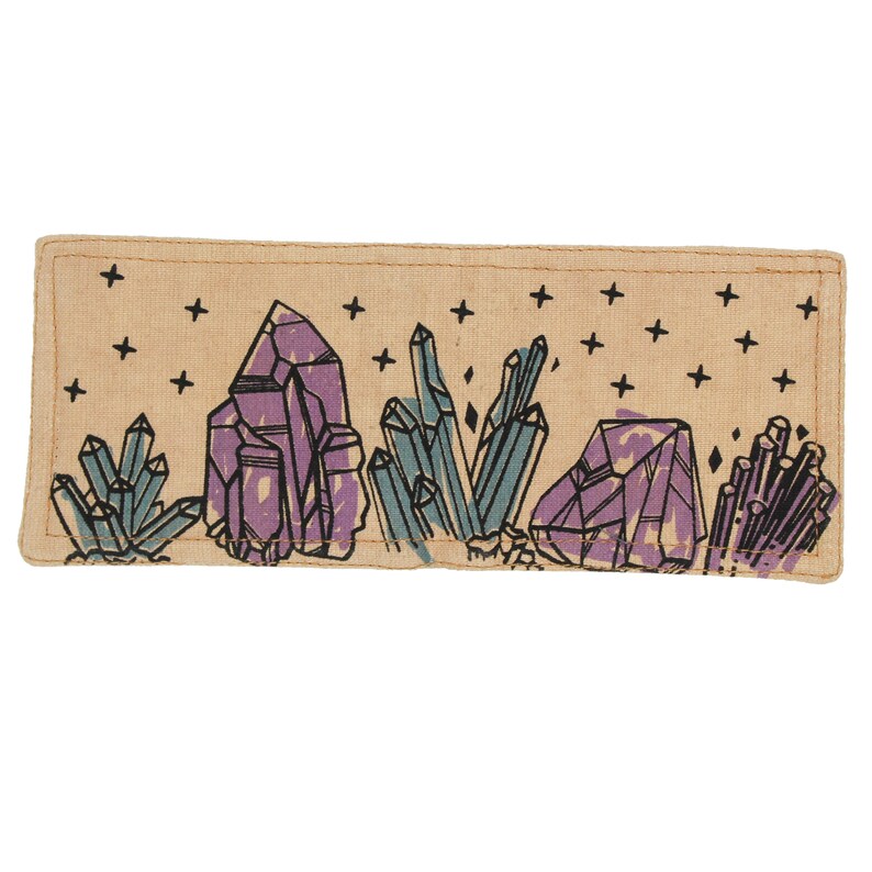 Pu&ograve; includere: Un cerotto in tessuto beige con un disegno di cristalli viola e blu su uno sfondo beige con stelle nere.