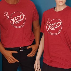 May include: Two red short-sleeved t-shirts featuring a white circular graphic of a bomb with a lit fuse. Inside the circle, the text reads RED, with the smaller text Reliable Excavation Demolition printed along the bottom curve of the circle.
