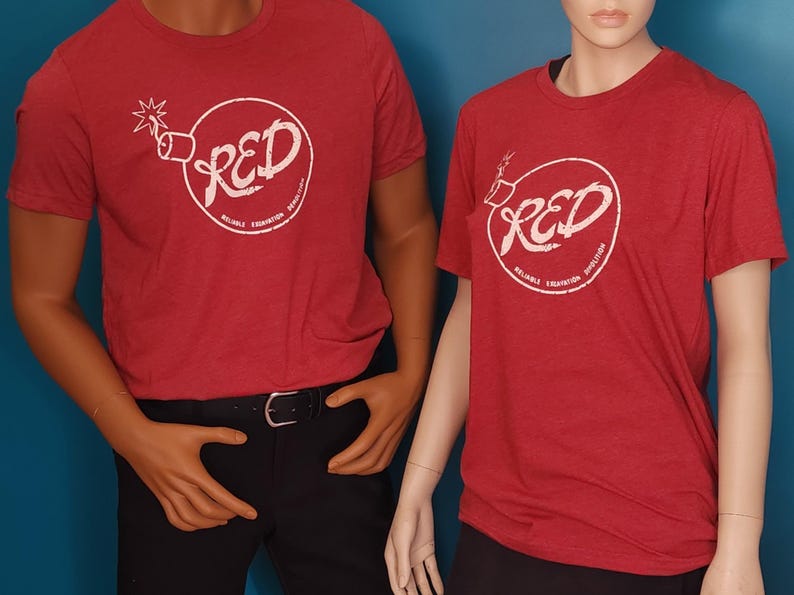 May include: Two red short-sleeved t-shirts featuring a white circular graphic of a bomb with a lit fuse. Inside the circle, the text reads RED, with the smaller text Reliable Excavation Demolition printed along the bottom curve of the circle.