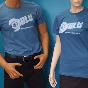 May include: Two blue short-sleeved t-shirts featuring a white graphic print on the chest. The design includes a stylized wrench forming the letter B, the text BLU, and the words BUILDERS LEAGUE UNITED in a distressed, weathered font style.