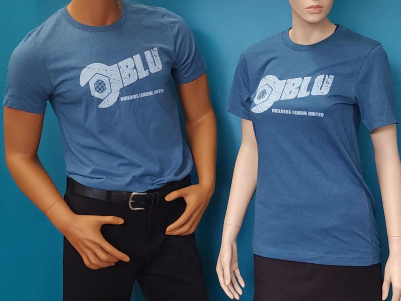 May include: Two blue short-sleeved t-shirts featuring a white graphic print on the chest. The design includes a stylized wrench forming the letter B, the text BLU, and the words BUILDERS LEAGUE UNITED in a distressed, weathered font style.