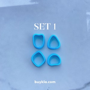 Puede incluir: Conjunto de cuatro cortadores de galletas de pl&aacute;stico azul en diferentes formas. Las formas son un coraz&oacute;n, un c&iacute;rculo, un cuadrado y un tri&aacute;ngulo. El texto "SET 1" est&aacute; escrito encima de los cortadores. El texto "buykla.com" est&aacute; escrito debajo de los cortadores.