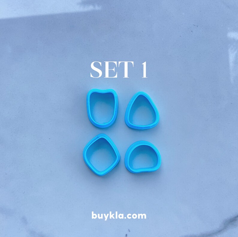 Puede incluir: Conjunto de cuatro cortadores de galletas de pl&aacute;stico azul en diferentes formas. Las formas son un coraz&oacute;n, un c&iacute;rculo, un cuadrado y un tri&aacute;ngulo. El texto "SET 1" est&aacute; escrito encima de los cortadores. El texto "buykla.com" est&aacute; escrito debajo de los cortadores.