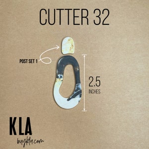 May include: A white and black polymer clay cutter shaped like an oval with a hole in the middle. The cutter is 2.5 inches tall. The text "CUTTER 32" is written above the cutter. The text "POST SET 1" is written to the left of the cutter. The text "KLA buykla.com" is written below the cutter.