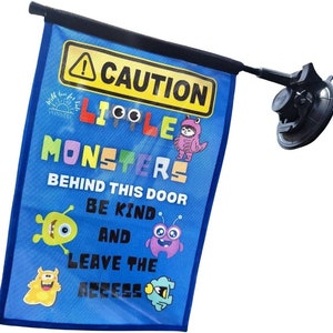 May include: Blue car window flag with the text "CAUTION LITTLE MONSTERS BEHIND THIS DOOR BE KIND AND LEAVE THE ACCESS". The flag features cartoon monster illustrations and a suction cup for attachment.