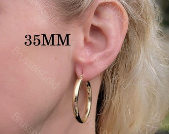 May include: Gold hoop earrings with a diameter of 35mm. The earrings are shown on a person's ear.